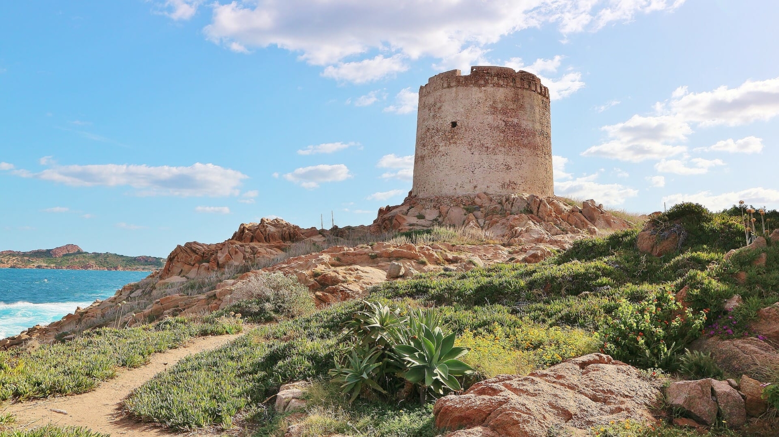 La rovina di una torre si erge su una collina e sullo sfondo si può vedere il mare