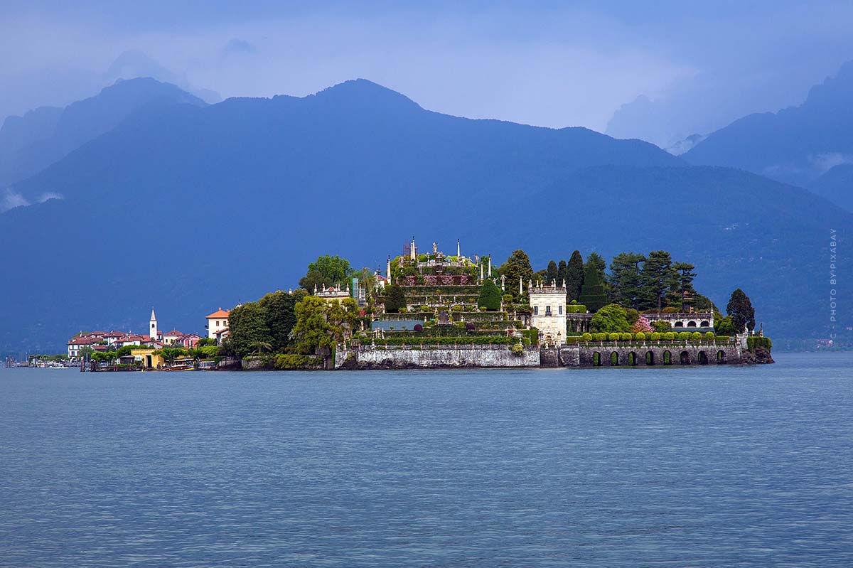 Un'isola con una villa e un giardino si trova nel lago davanti ai contorni blu delle montagne.