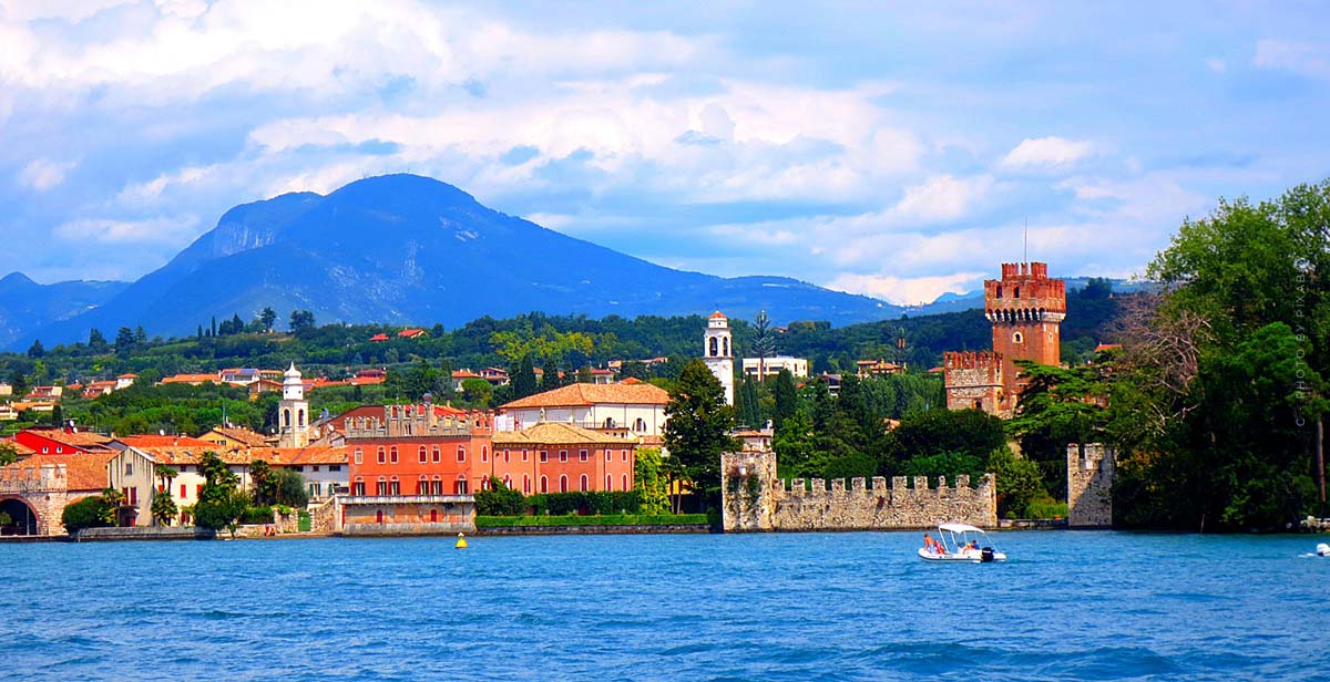 Una città si trova sulla riva di un lago blu e sullo sfondo si vede una montagna.