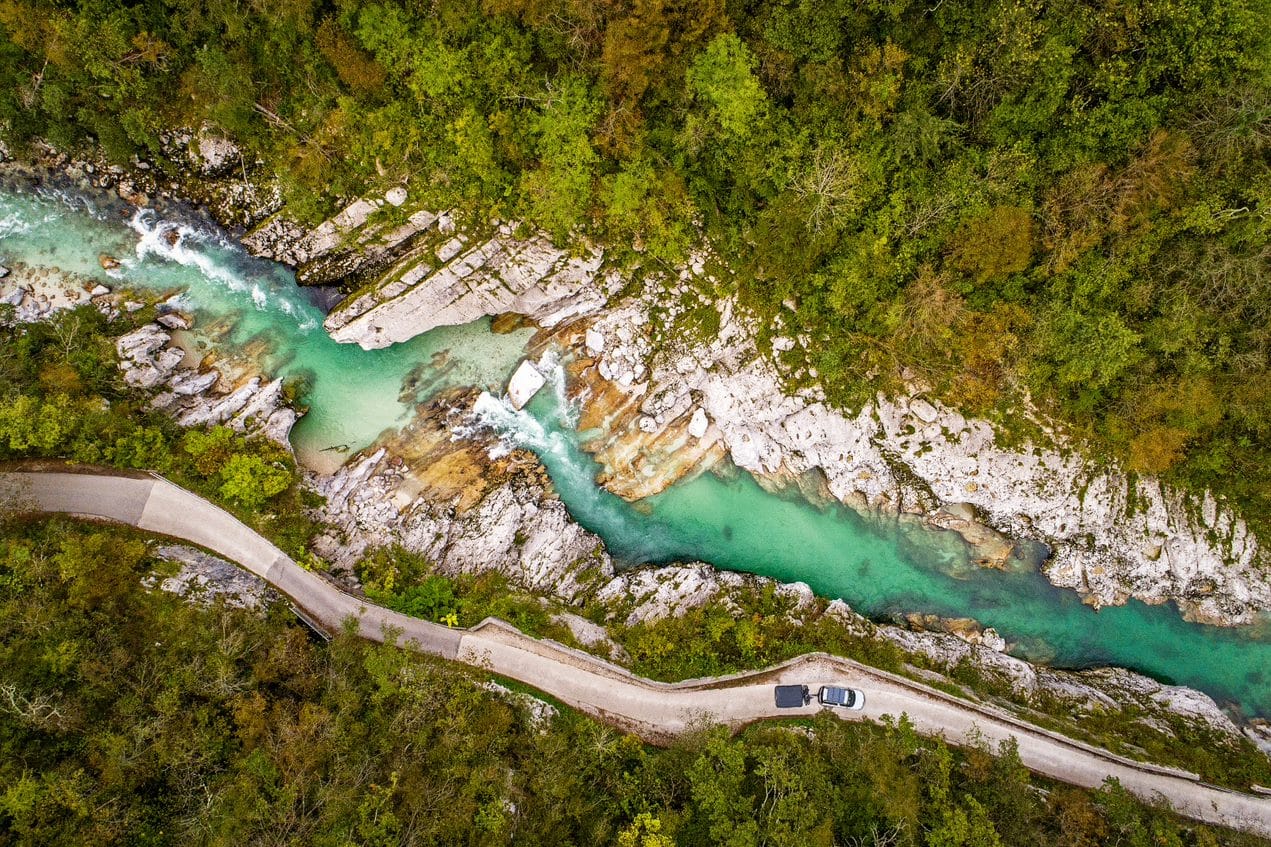 Con tenda da tetto e rimorchio tenda attraverso la natura selvaggia: un'auto percorre una strada solitaria tra gli alberi lungo un fiume.