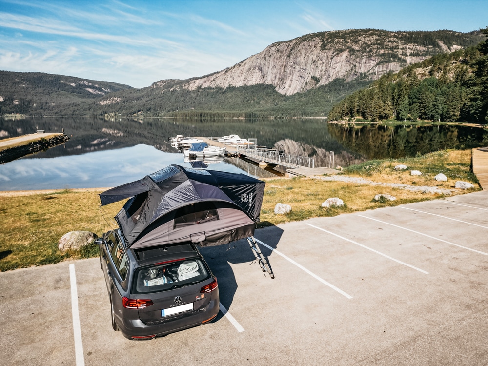 Un'auto con tenda da tetto aperta si trova in un parcheggio al lago: Campeggiare al di fuori dei campeggi non è solo per gli avventurieri. Foto: femaleglobetrotter/CAMPWERK