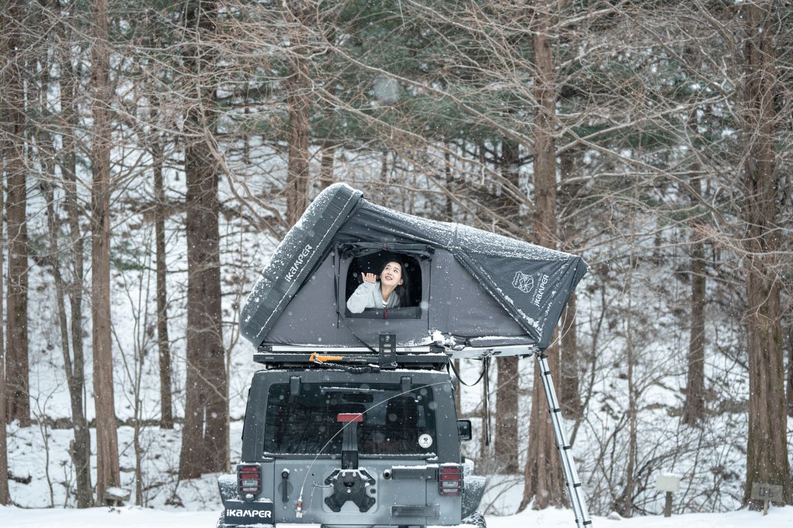 Donna che si gode la neve intorno alla sua tenda da tetto Skycamp in inverno