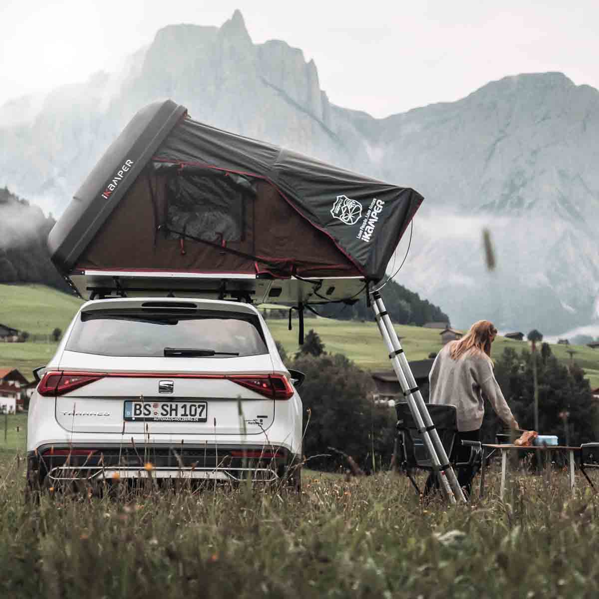Donna in montagna accanto alla sua auto con tenda da tetto