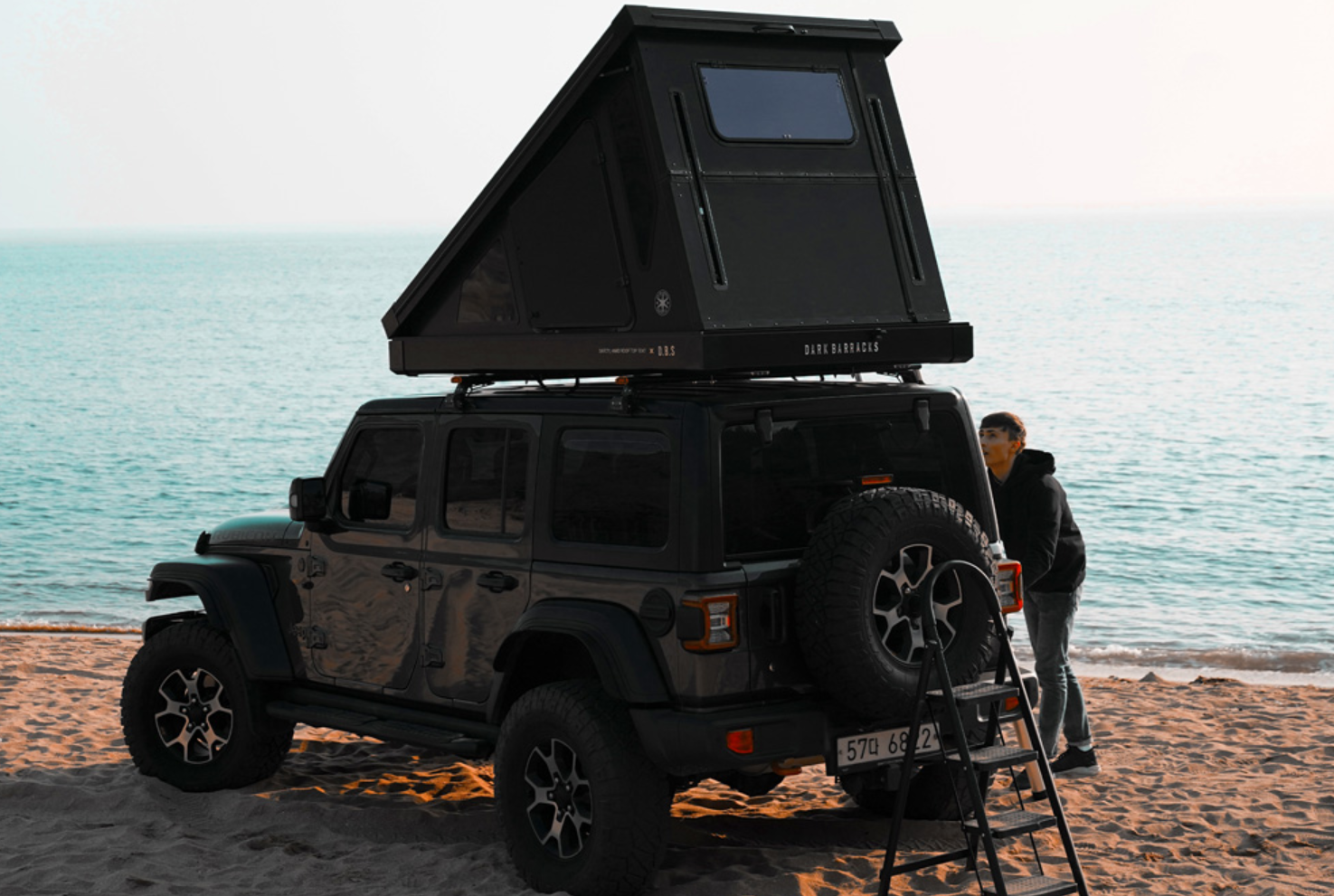 Uomo che allestisce il suo campeggio accanto alla sua auto con tenda da tetto Dark Barracks Hardside