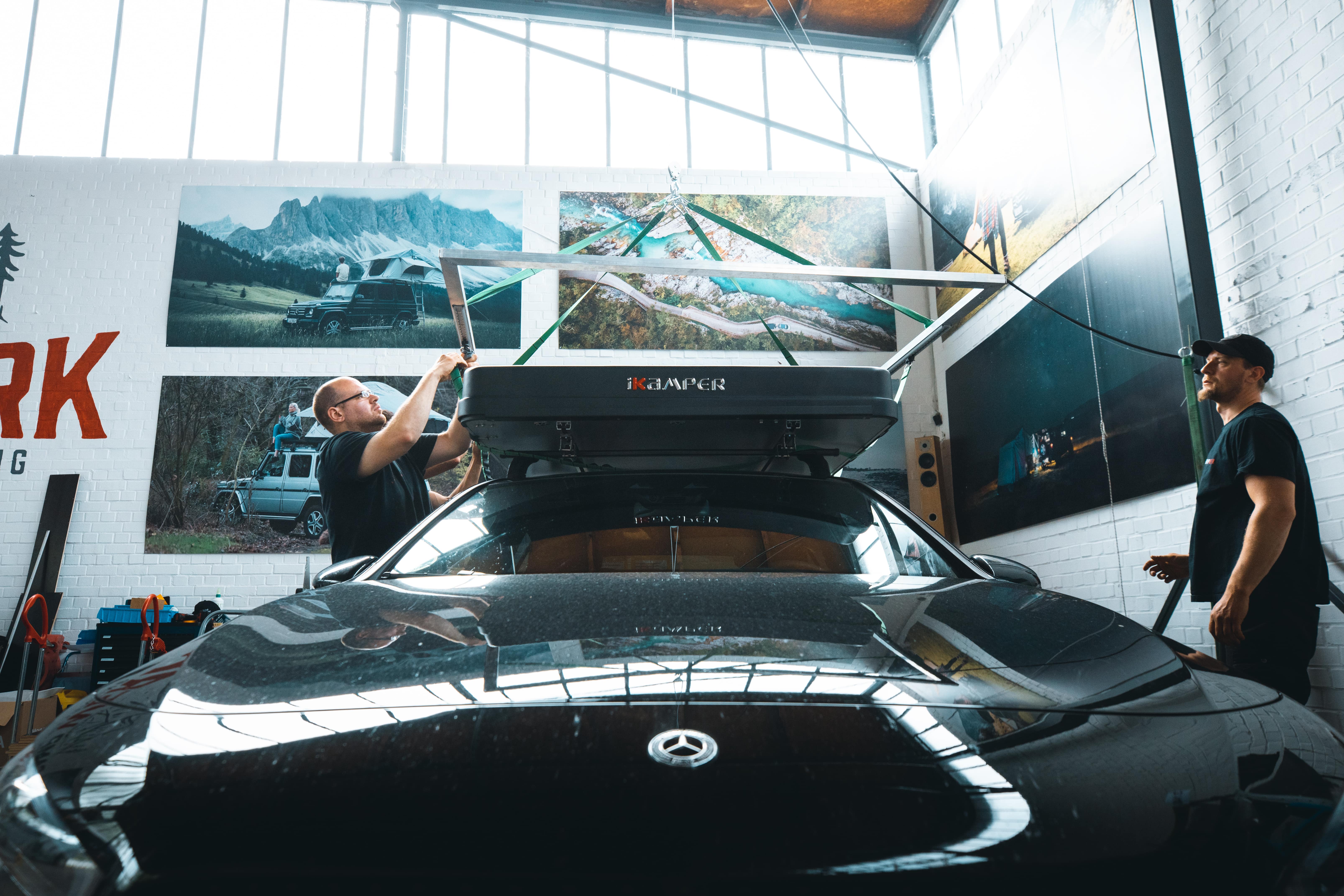 Dipendenti di Campwerk montano una tenda da tetto su un'auto nera