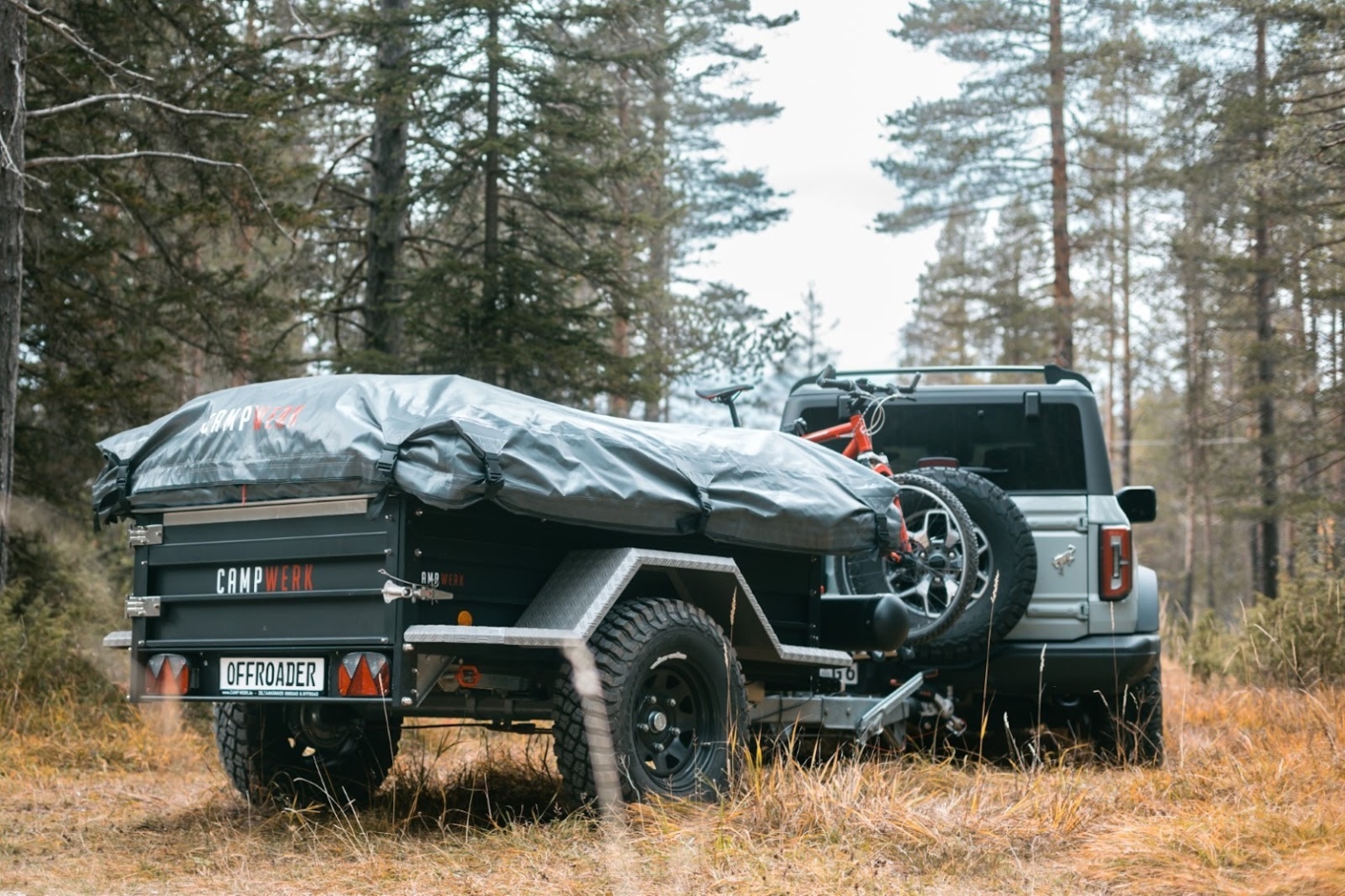 Un'auto con un rimorchio tenda staccato su un sentiero forestale