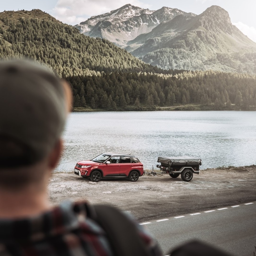 Persona che guarda un'auto con un rimorchio tenda staccato sul lago